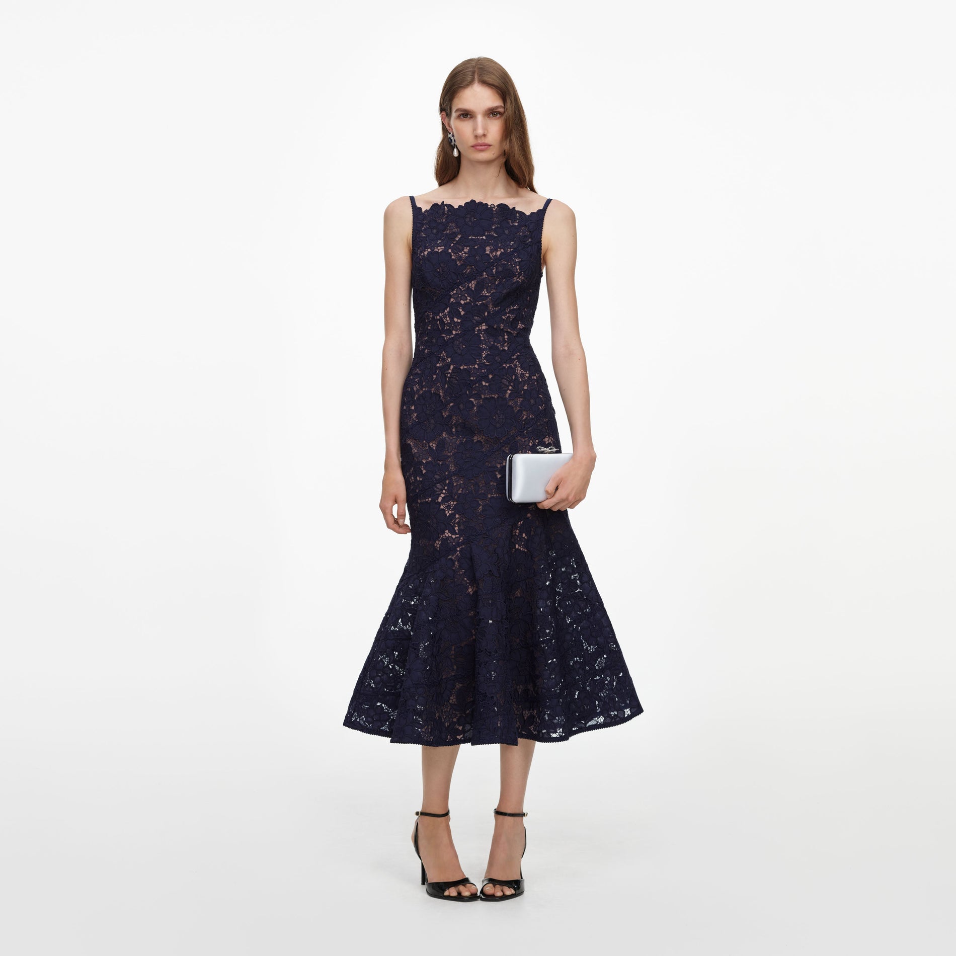 Woman in a navy blue lace midi dress with a scalloped neckline, holding a silver clutch