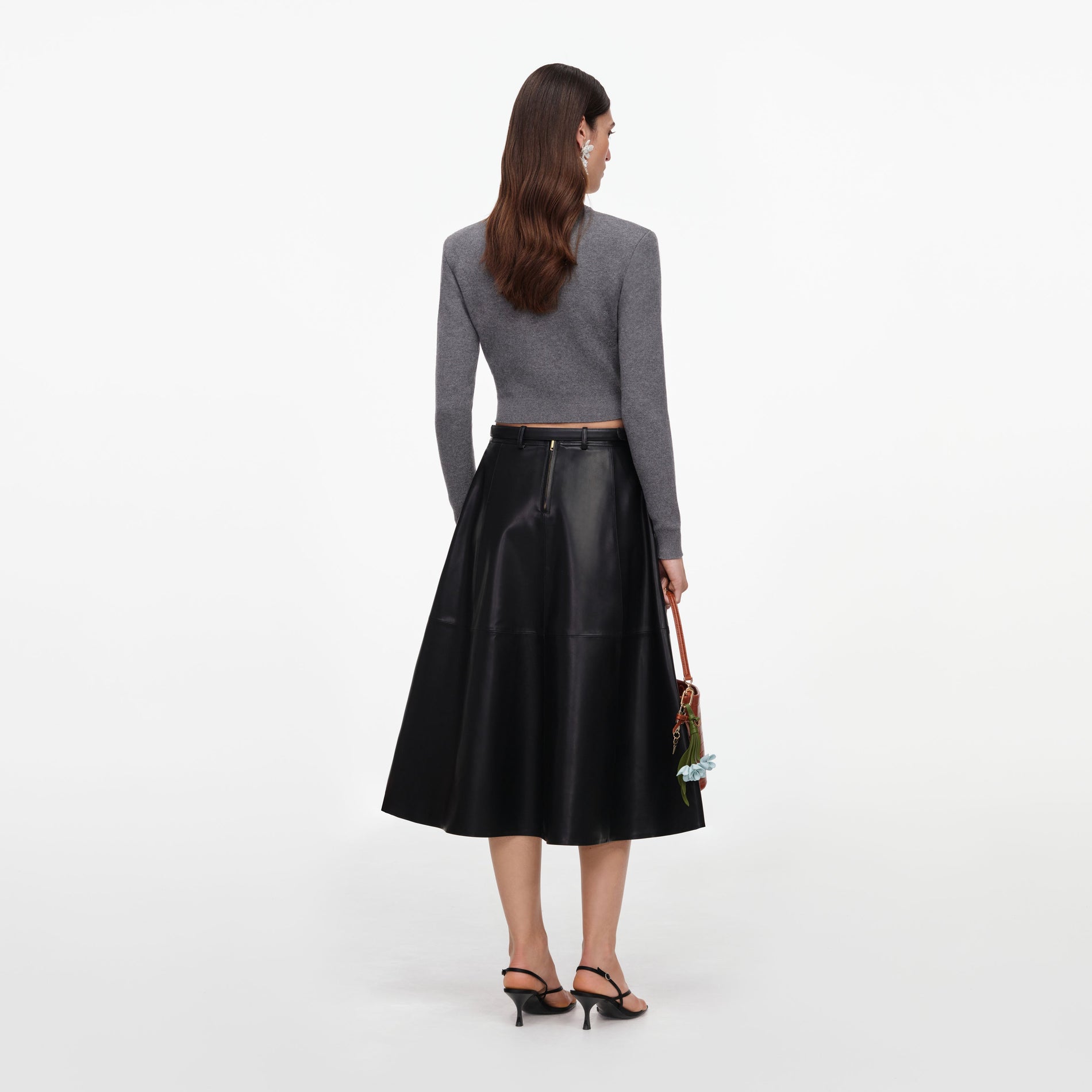 Woman in grey long-sleeve top, black leather midi skirt, black heels, and brown handbag with blue flowers