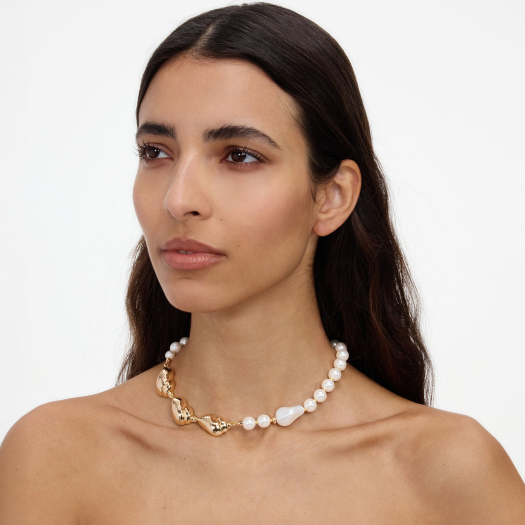 A close up of a woman wearing the Gold Shell And Pearl Necklace