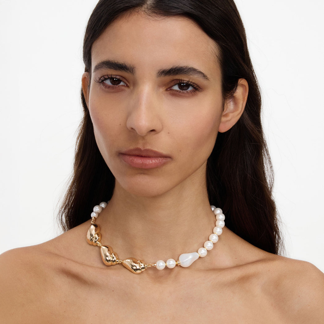 A close up of a woman wearing the Gold Shell And Pearl Necklace