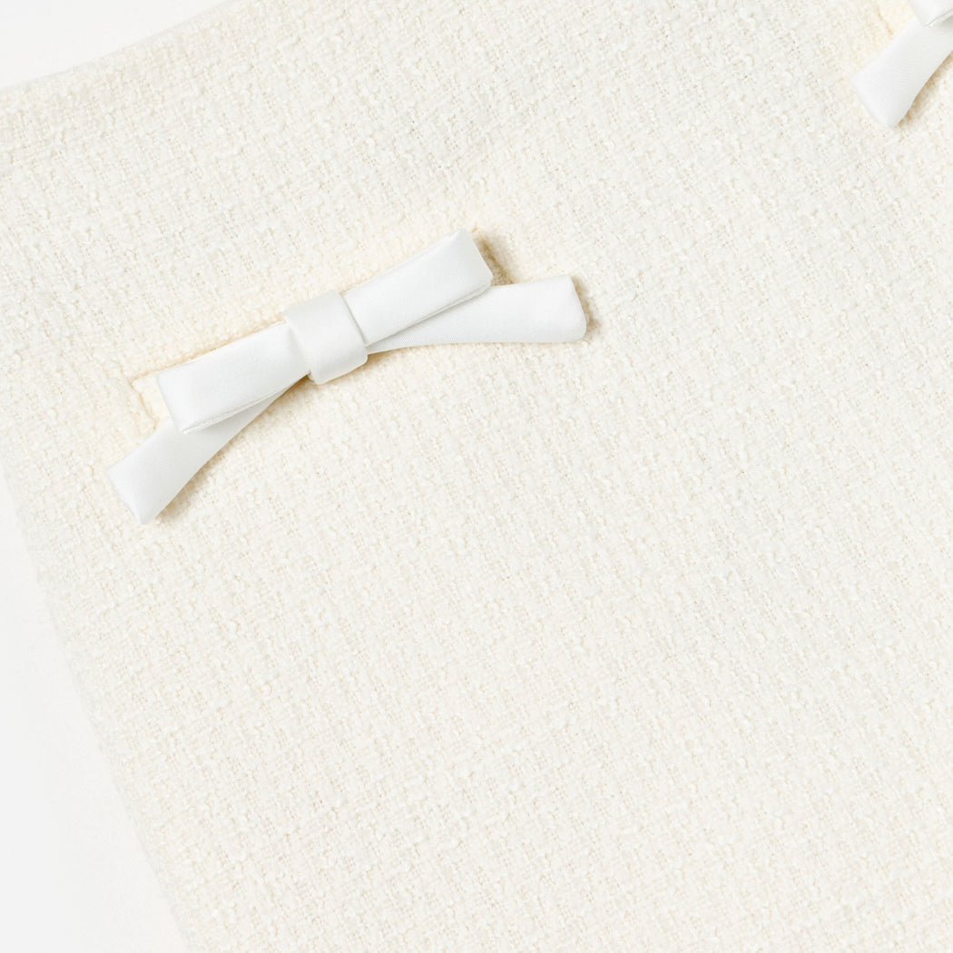 Close-up of a cream-colored textured fabric with two white satin bows