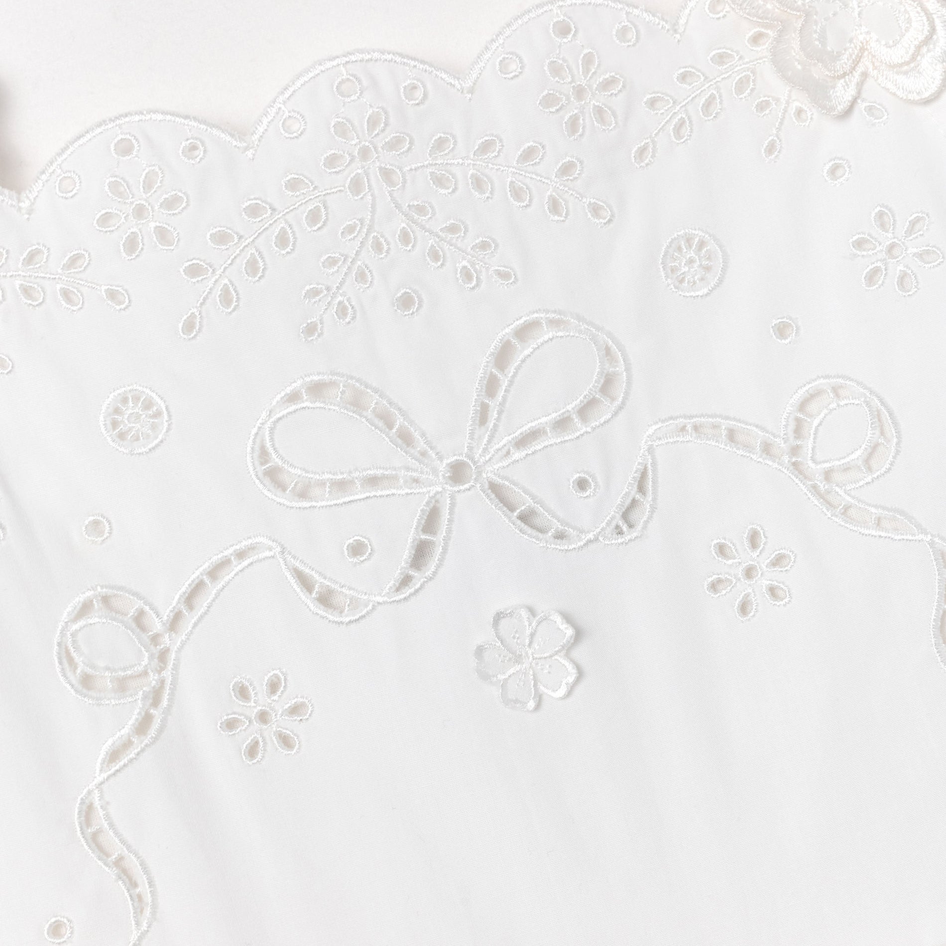 White fabric with embroidered scalloped edge, floral patterns, and a large bow design