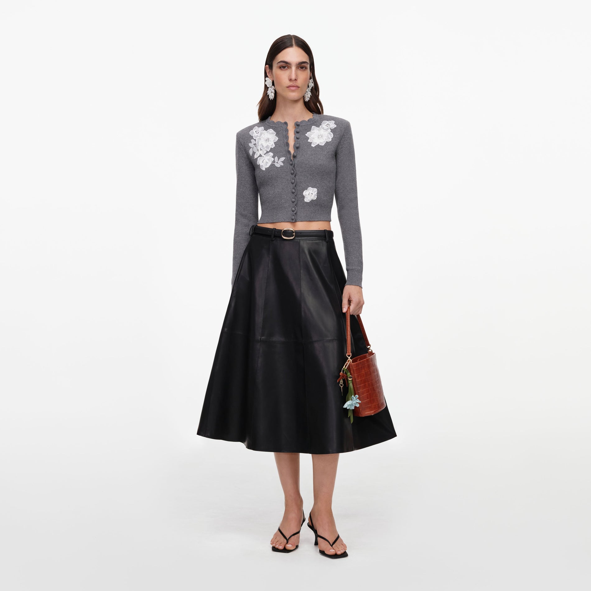 Woman in a grey floral cardigan, black leather skirt, black sandals, and a brown handbag