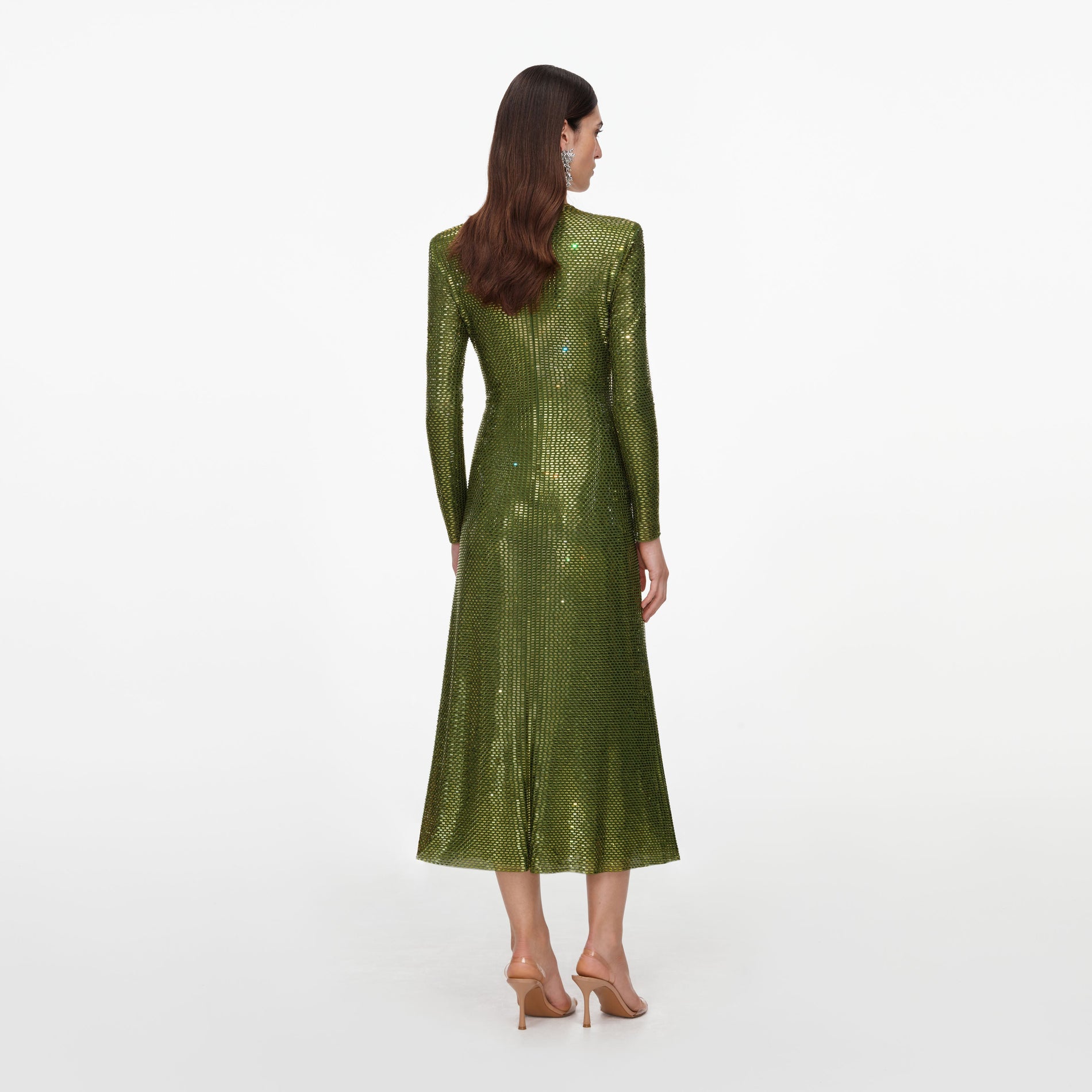 Woman in a green sequined midi dress with long sleeves and pointed shoulders, facing away from the camera