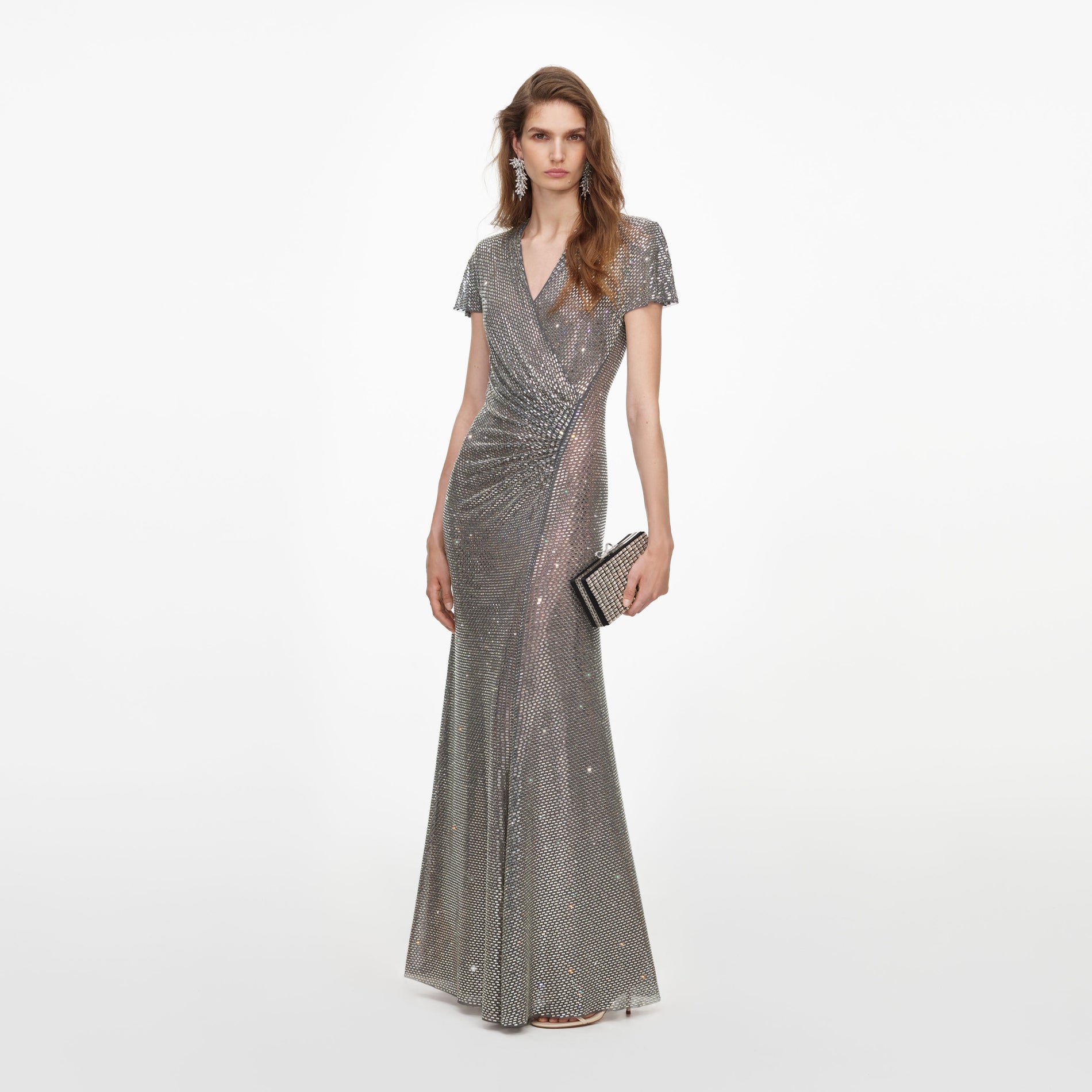 Woman in a silver sequin gown with short sleeves, V-neck, and a ruched waist, holding a matching clutch