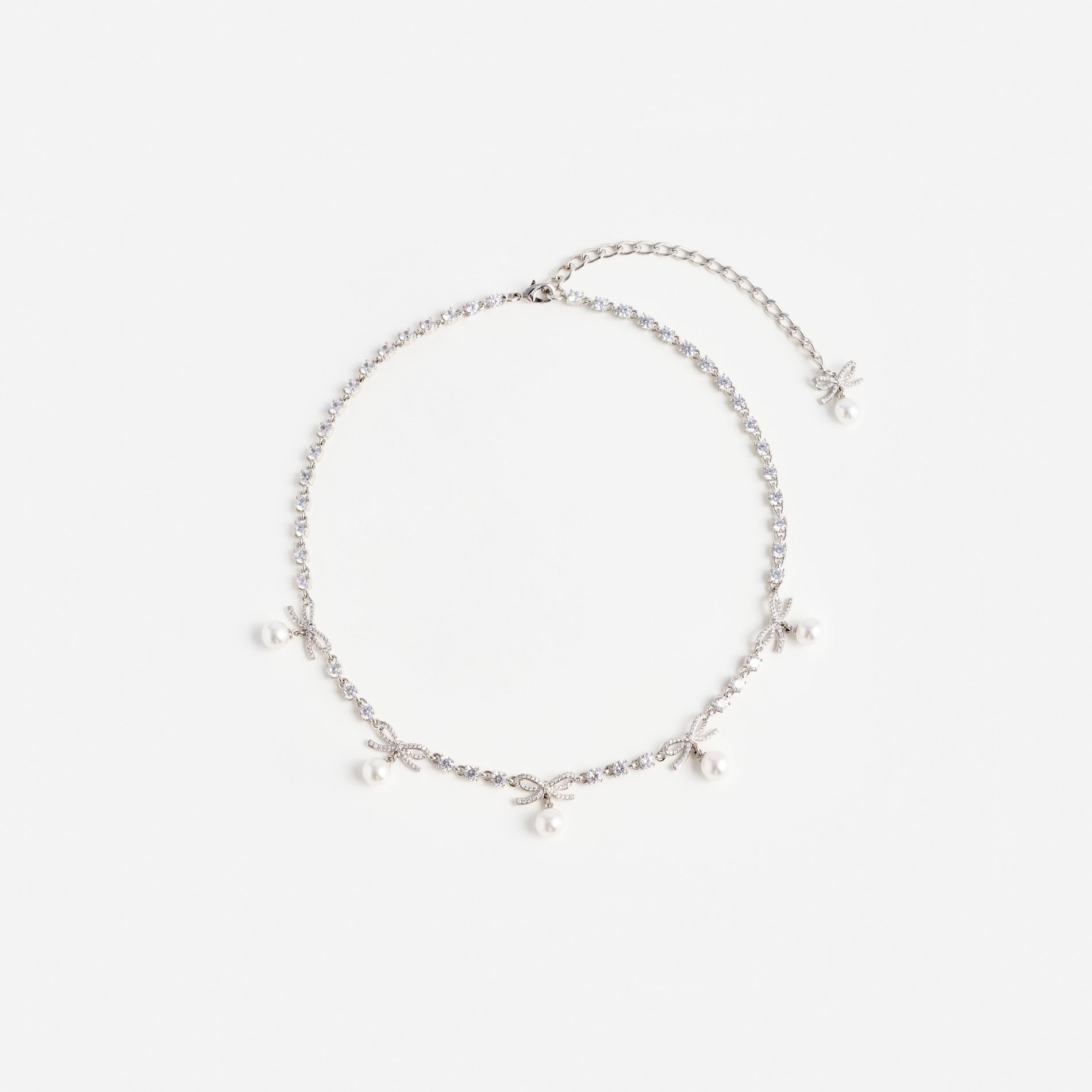 Silver necklace with small clear stones, five bow-shaped charms, and five small white pearls