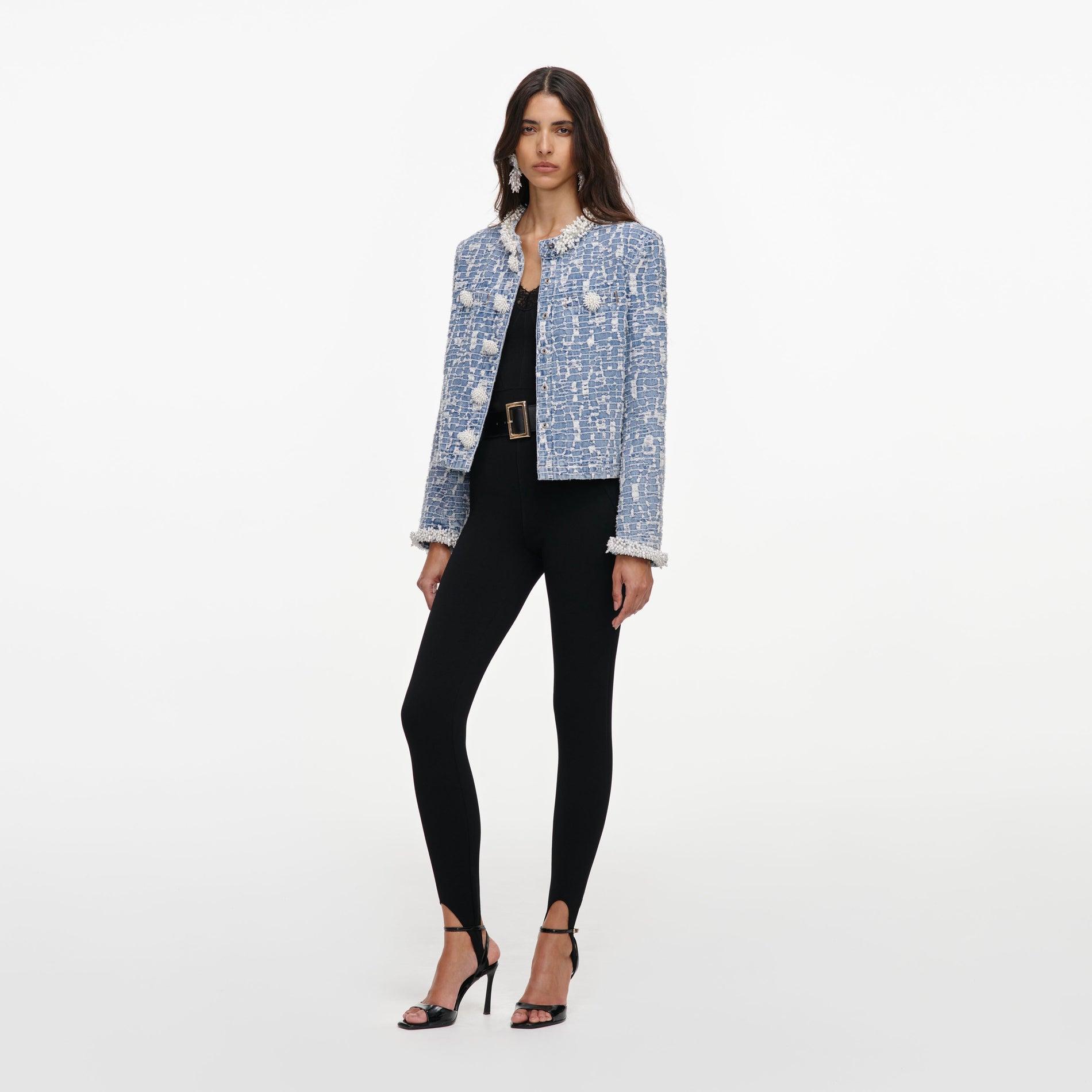 Woman wearing a blue tweed jacket with pearl details, black top, black stirrup leggings, and black heels