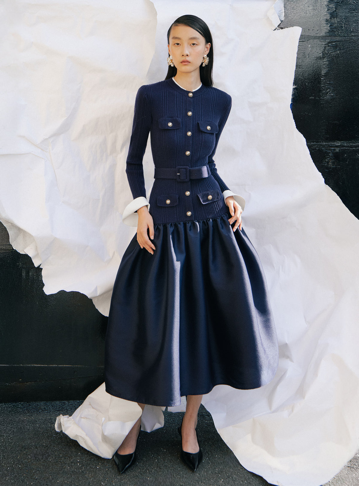 Woman wearing a navy blue belted dress with gold buttons and a full skirt