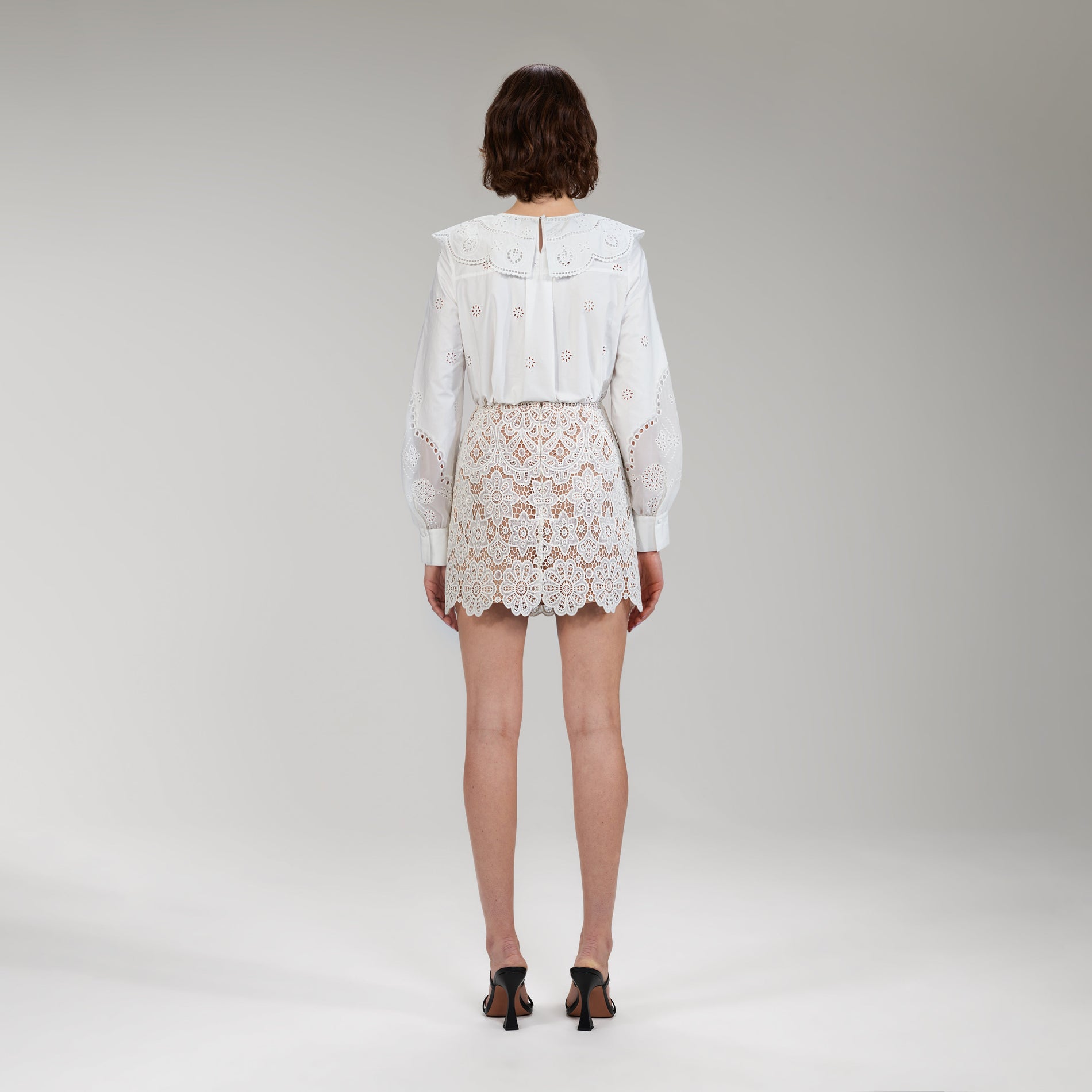 A woman wearing the Ivory Floral Guipure Mini Skirt