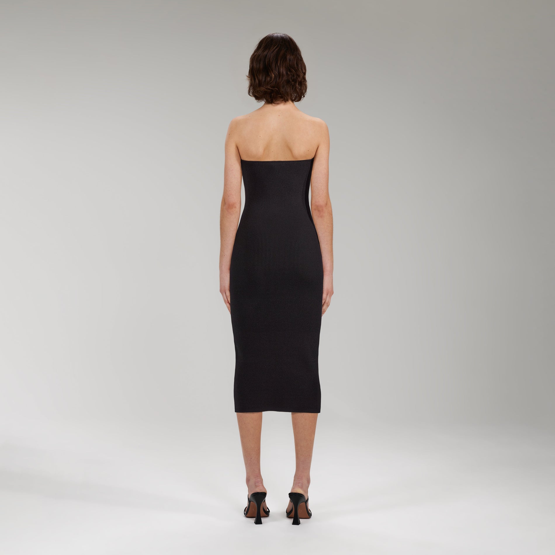 A woman wearing the Black Strapless Ribbed Knit Midi Dress