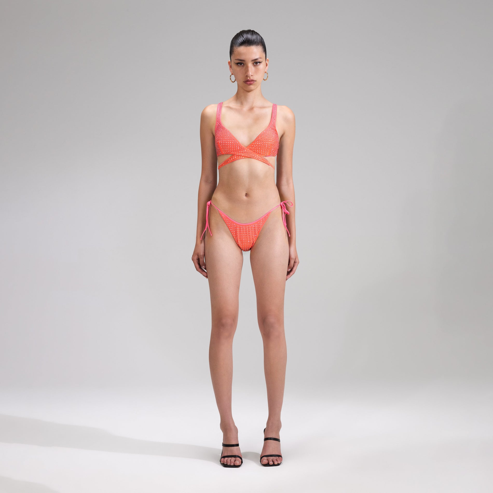 A woman wearing the Orange Rhinestone Tie Side Bikini Brief