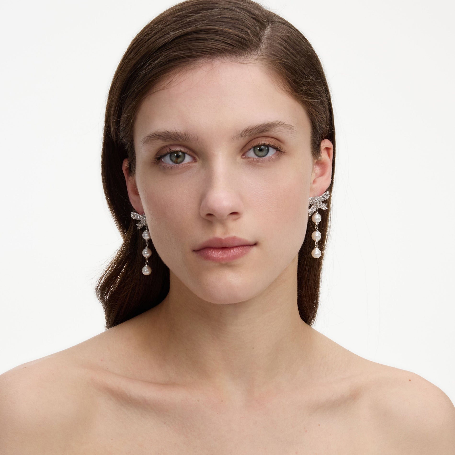 A close up of a woman wearing the Crystal Bow Pearl Droplet Earrings