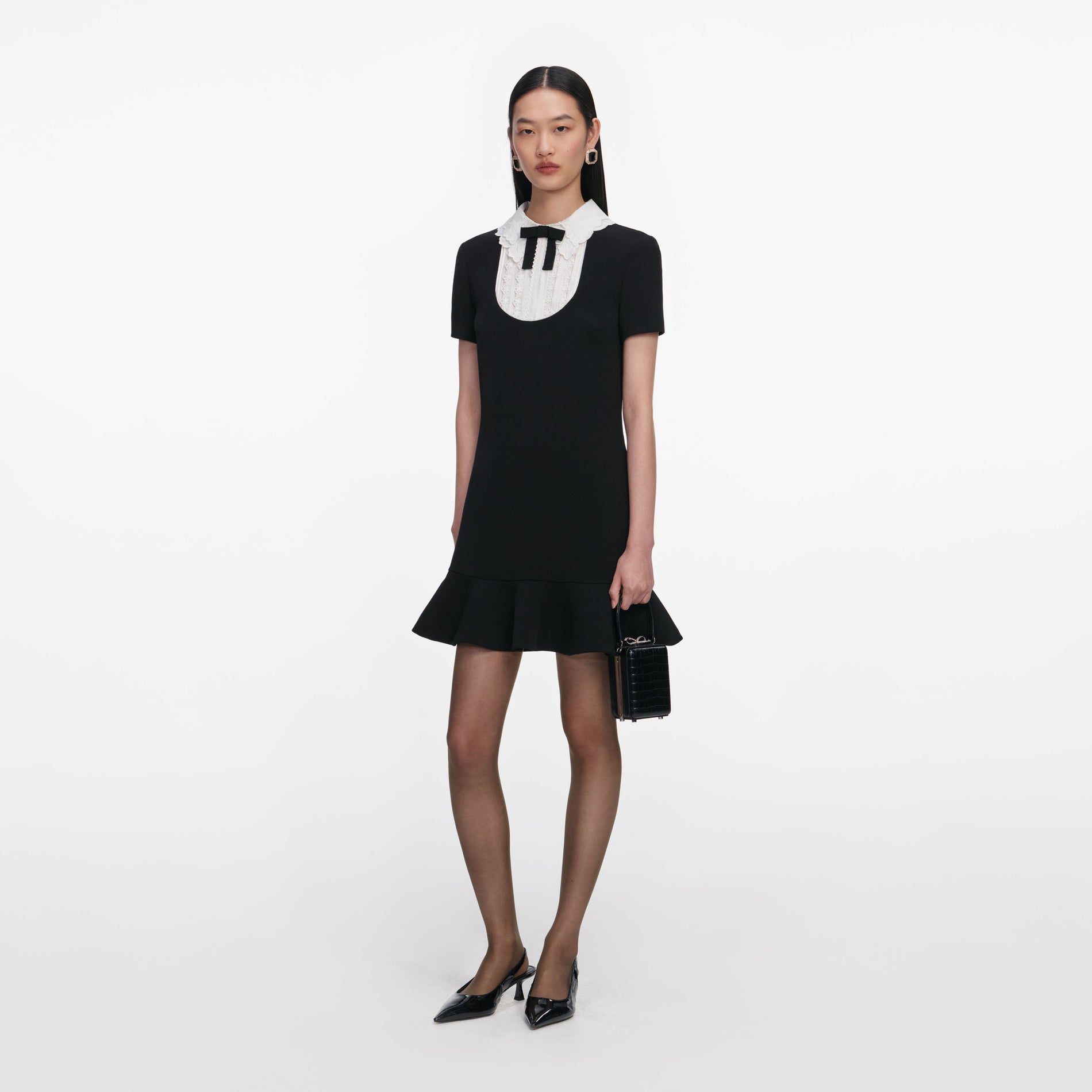 Side view of a woman wearing the Black Crepe Lace Bib Mini Dress