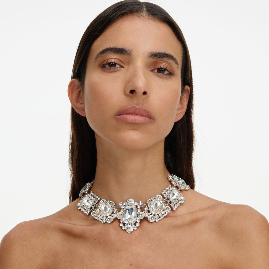 Woman with long dark hair wearing a large, ornate crystal choker necklace