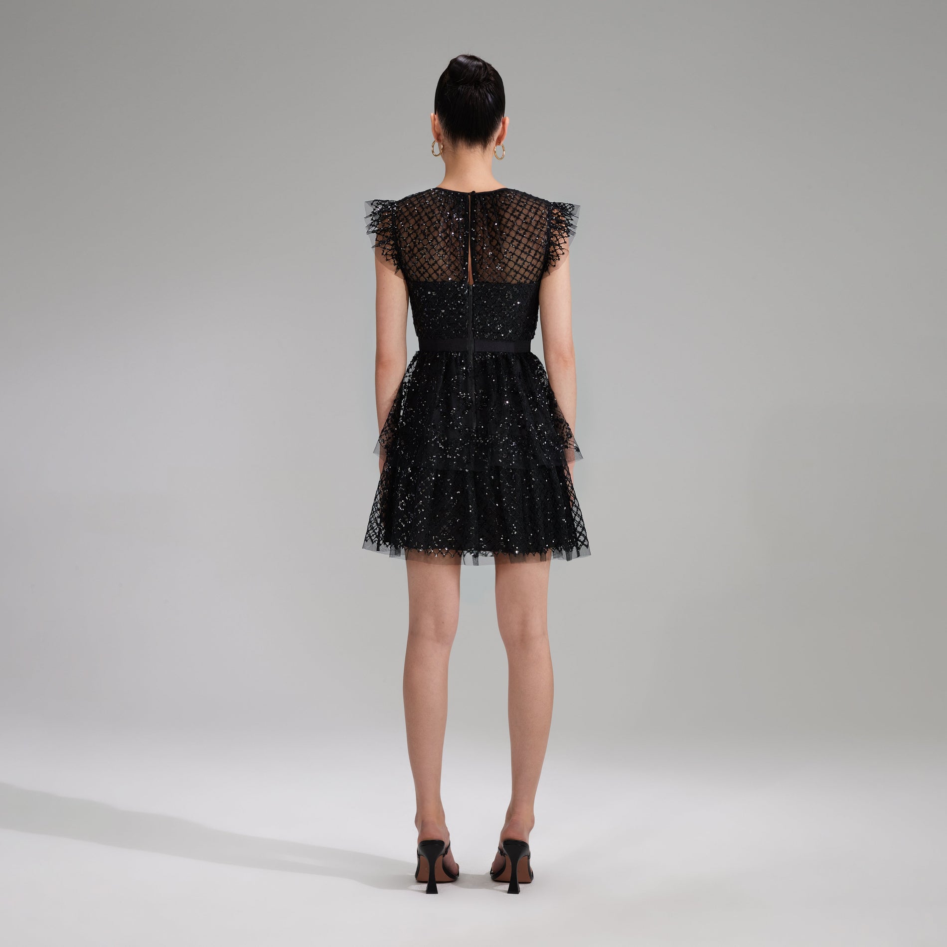 A woman wearing the Black Grid Sequin Tiered Mini Dress